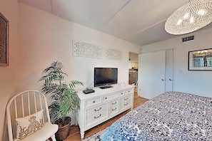 A bedroom with a bed, a television on a dresser, a potted plant, and a door leading to another room. - Surfside I Condominiums #301 (South Padre Island)