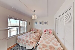 A bedroom with two beds, a window with a view, a hanging light fixture, and a set of lockers. - Surfside I Condominiums #301 (South Padre Island)