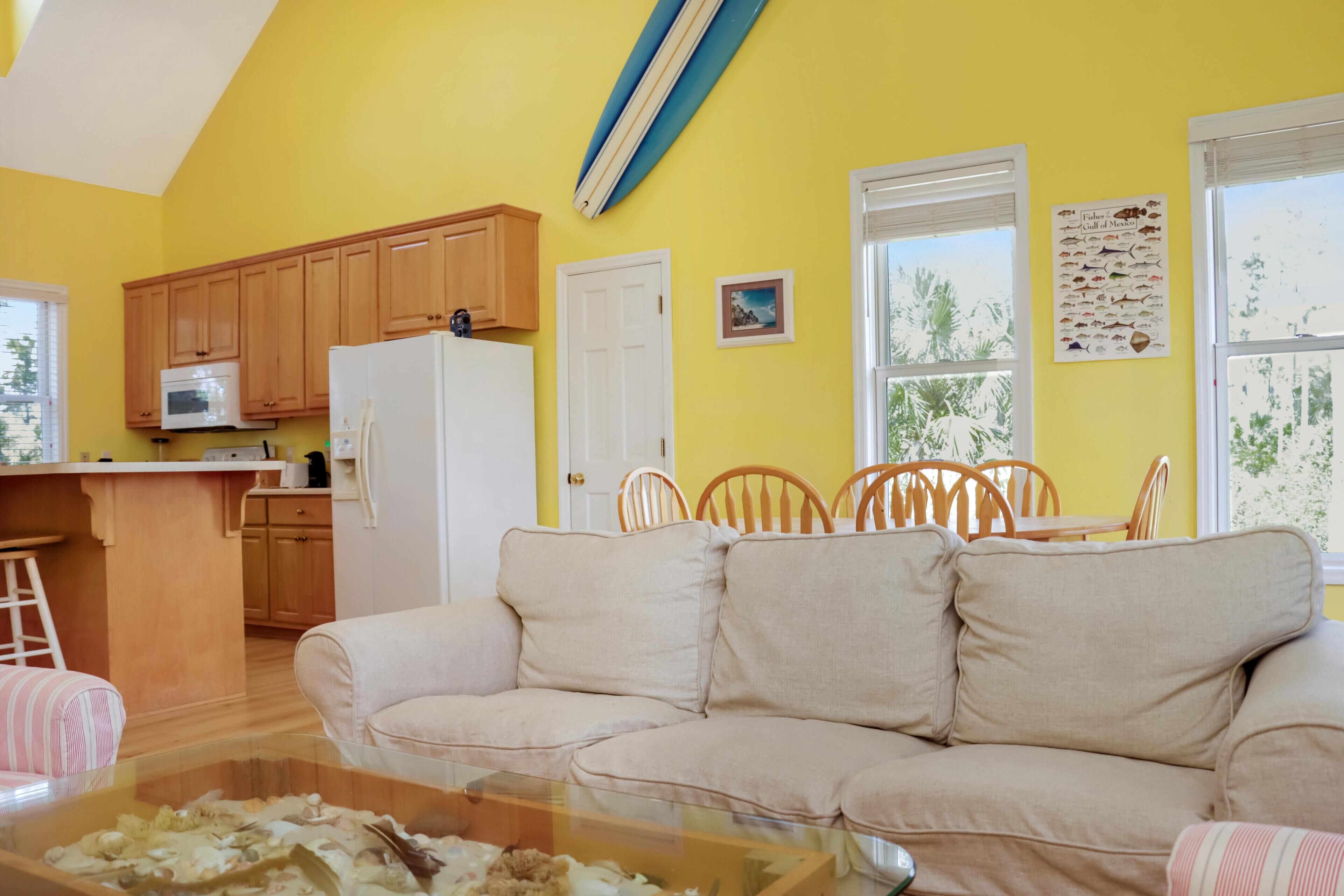 A bright yellow interior with a kitchen, a dining area, and a living room with a sofa and a glass coffee table.