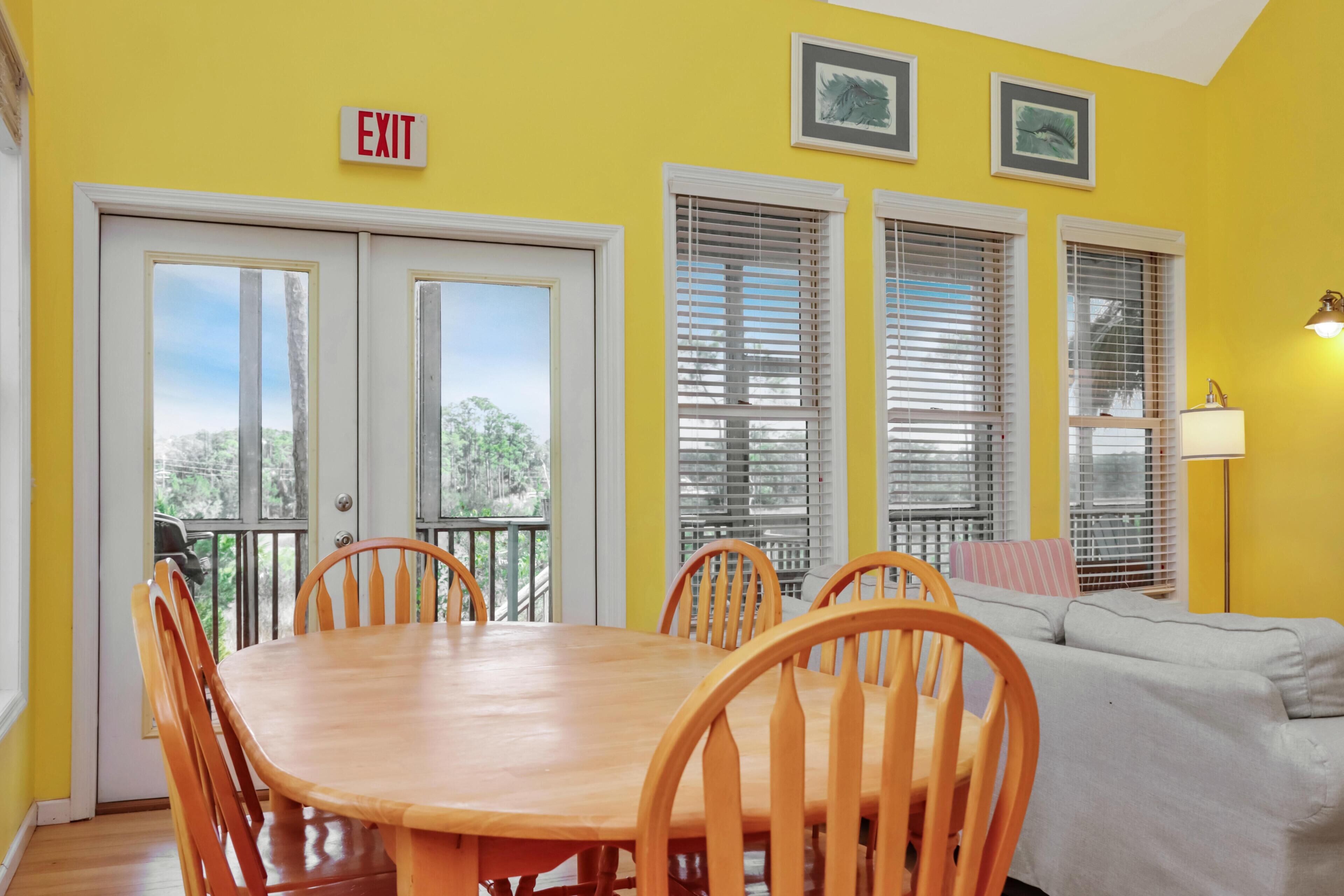 A dining area with a wooden table and chairs, a sofa, and a balcony with a view.