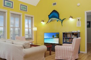 Ein Wohnzimmer mit einem großen Flachbildfernseher, einem Bücherregal, einem gestreiften Sessel und einem Sofa.