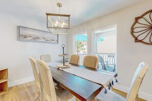 A dining area with a wooden table, six chairs, a chandelier, a framed picture, and a balcony with a railing. - Carolyn's Beach House unit A (South Padre Island)