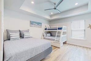 A bedroom with a bunk bed, a single bed, a ceiling fan, and a window with blinds. - Carolyn's Beach House unit A (South Padre Island)