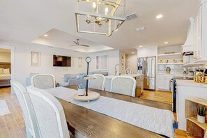 A modern kitchen with white cabinets, a stainless steel refrigerator, and a dining area with a wooden table and chairs. - Carolyn's Beach House unit A (South Padre Island)