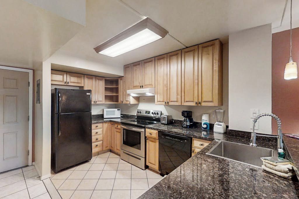 A kitchen with wooden cabinets, a black refrigerator, a microwave, a stove, and a sink.