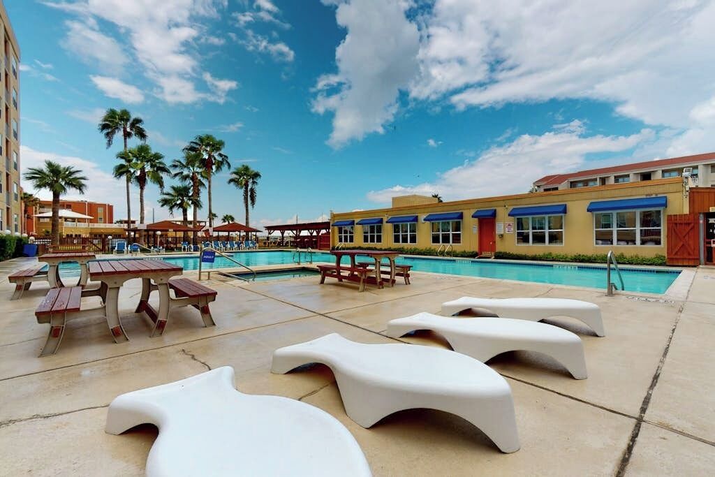 A poolside area with lounge chairs, a pool, and a building with blue awnings.