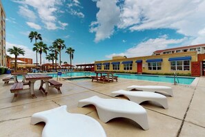 A poolside area with lounge chairs, a pool, and a building with blue awnings. - Gulfview I #312 - Ocean View & Hot Tub (South Padre Island)