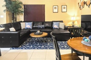 A living room with a black leather sofa, a round wooden coffee table, and a blue patterned rug. - Kingfisher - Shared Pool, Walk to the Beach (South Padre Island)
