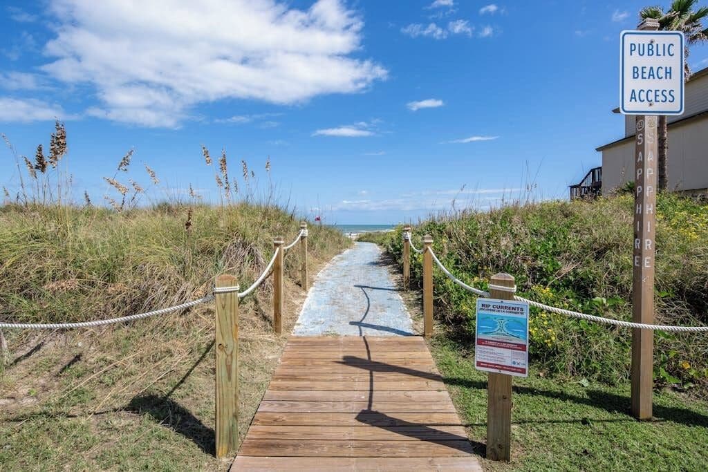 A wooden boardwalk leading to a beach with a sign indicating public beach access.