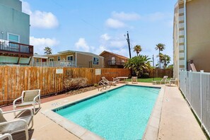 A rectangular swimming pool with lounge chairs and a wooden fence. - Escape Condominiums #2 (South Padre Island)
