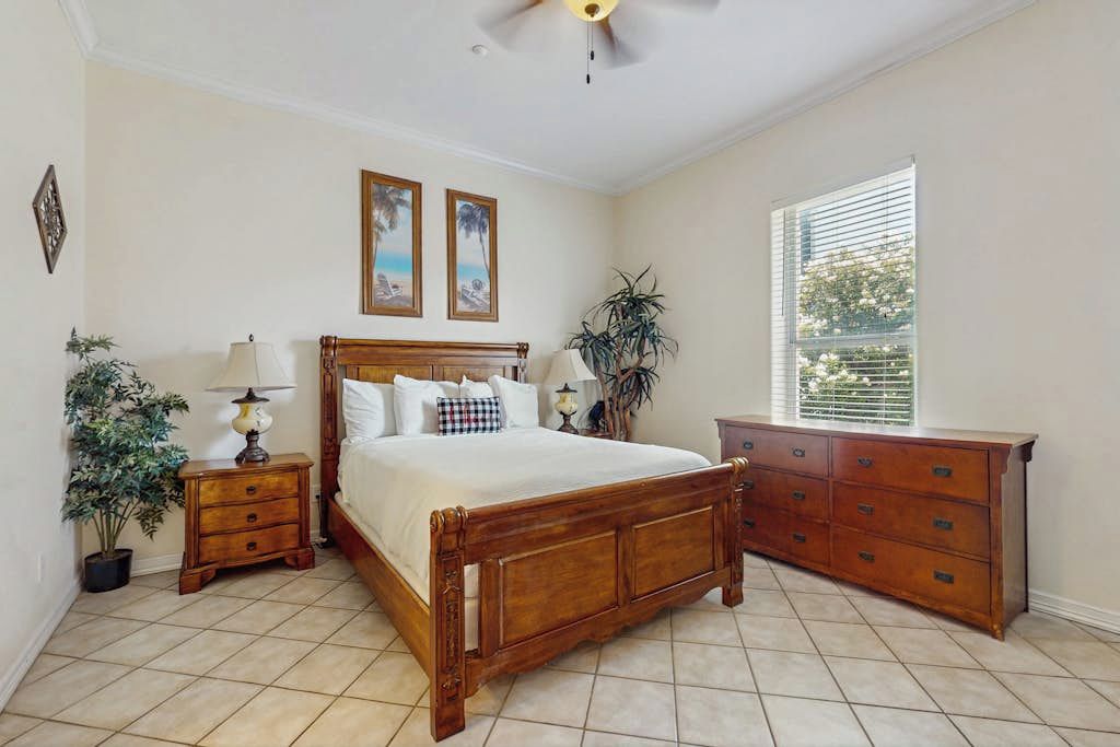 A bedroom with a wooden bed, bedside tables, a dresser, and a window with blinds.