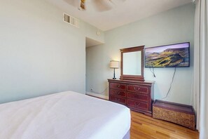 Una camera da letto con un letto, una cassettiera, uno specchio e una TV a parete.