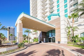 A hotel entrance with a covered walkway, palm trees, and a modern building with balconies. - Sapphire Condominiums Bungalow #106 (South Padre Island)