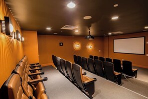 Cine con filas de asientos negros, una pantalla grande e iluminación instalada en la pared.