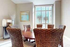 A dining area with a round table and wicker chairs, a vase with branches, and a framed picture on the wall. - Sapphire Condominiums Bungalow #106 (South Padre Island)