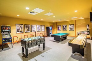 Una habitación con mesa de fútbol de mesa, mesa de billar y mesa de fútbol de mesa con superficie de mármol. Hay cuadros en la pared y un televisor a la derecha.