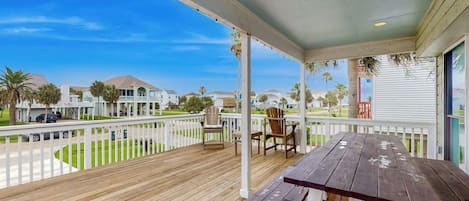 A wooden deck with a table and chairs, overlooking a residential area with houses and palm trees.