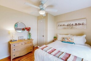 A bedroom with a bed, a dresser, a mirror, a ceiling fan, and a wall art piece. - Piper's Place - Short Walk to Beach, Dogs OK (Galveston)