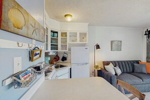 Eine kompakte Küche mit weißen Schränken, einem Kühlschrank und einer Essecke mit Tisch und einer Couch.