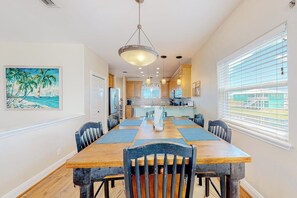 A dining area with a wooden table and chairs, a pendant light, and a painting on the wall. - Another Day In Paradise (Port Aransas)