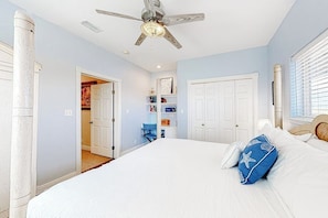 A bedroom with a large bed, a ceiling fan, and a door leading to another room. - Another Day In Paradise (Port Aransas)