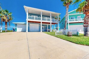 A two-story building with a balcony, a garage, and a fenced yard. - Another Day In Paradise (Port Aransas)