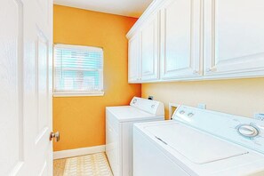 A laundry room with white cabinets, a washing machine, and a dryer. - Another Day In Paradise (Port Aransas)