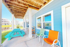 A covered patio with a wooden ceiling, a turquoise picnic table, and two chairs. - Another Day In Paradise (Port Aransas)