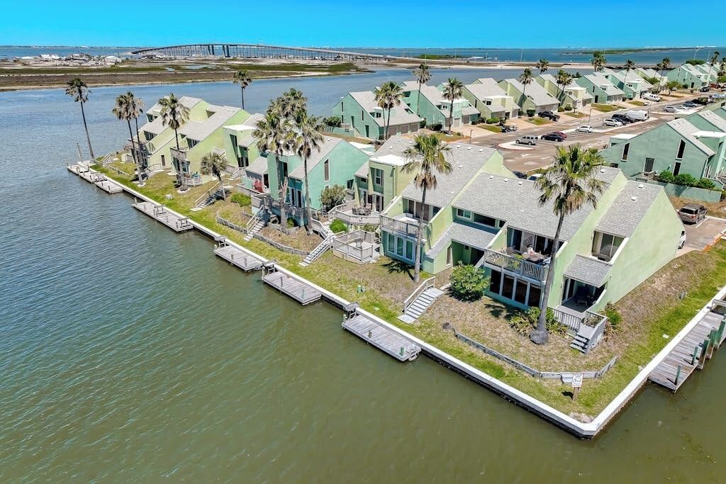 A waterfront property with multiple green-roofed buildings, docks, and palm trees.