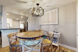 A dining area with a round wooden table and chairs, a chandelier, and a white cabinet with striped cushions. - Puente Vista 105 - Waterfront, Dock & Fire Pit (Corpus Christi)