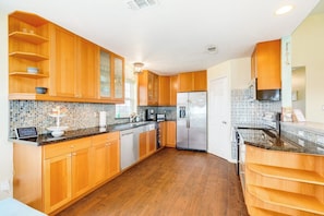 A kitchen with wooden cabinets, a stainless steel refrigerator, and a tiled backsplash. - Bayside Paradise - Private Pool & Bay Views (Galveston)
