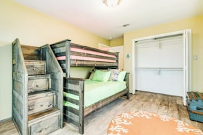 A bedroom with a bunk bed, a wooden dresser, a closet, and a patterned rug. - Bayside Paradise - Private Pool & Bay Views (Galveston)