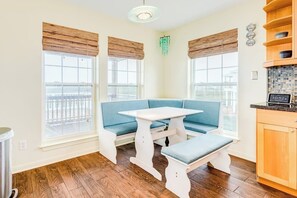A room with a blue sofa, a white table, and a bench. There are windows with wooden blinds and a view outside. - Bayside Paradise - Private Pool & Bay Views (Galveston)