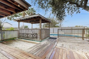 A wooden deck with a covered seating area, a pool, and a fence. - The Saltbox - Private Pool, Fire Pit & Yard (Corpus Christi)