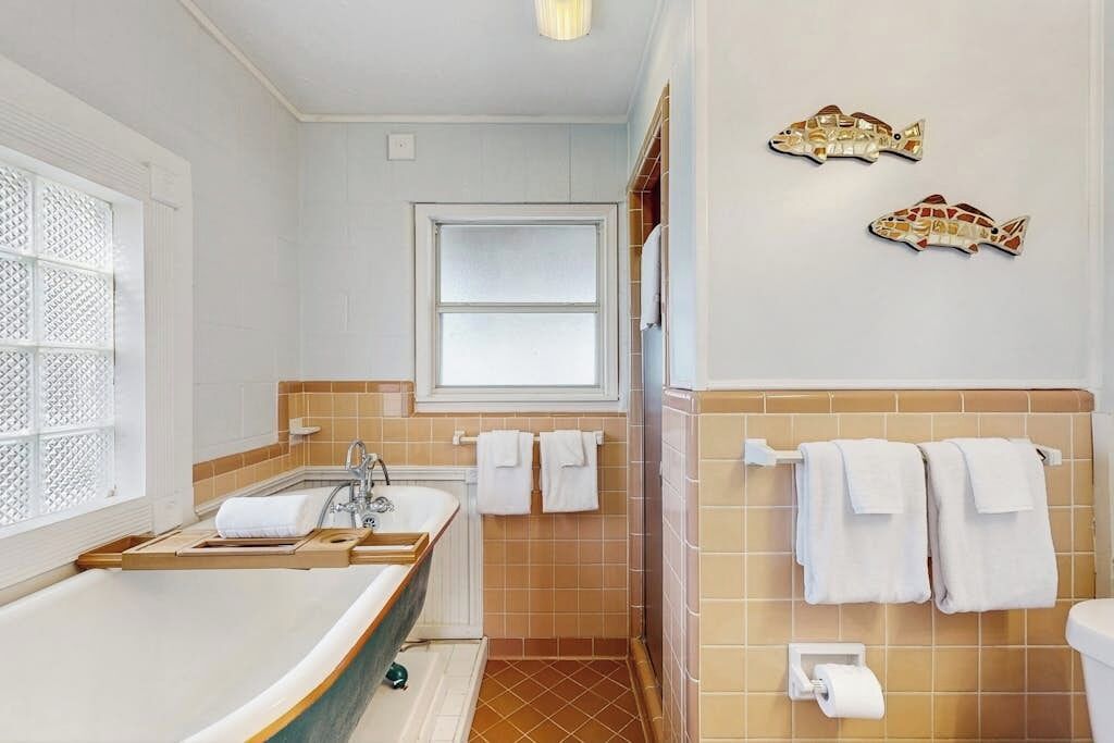 A bathroom with a bathtub, a window, and two fish-shaped wall decorations.