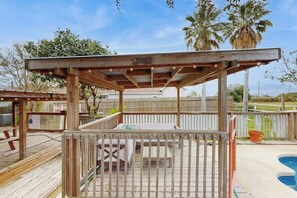 Um deck de madeira com pérgola, área de estar externa e piscina.