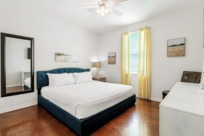 Habitación de hotel con cama, ventilador de techo, escritorio y ventana con cortinas.