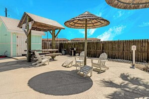 Eine Terrassenfläche mit Außenmöbeln, einem Reetdachschirm und einem Holzzaun.