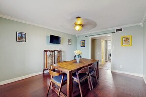 A dining area with a wooden table and chairs, a ceiling fan, and framed artwork on the walls. - Sunshine Shores - Pool Table, Yard & Dogs OK (Corpus Christi)