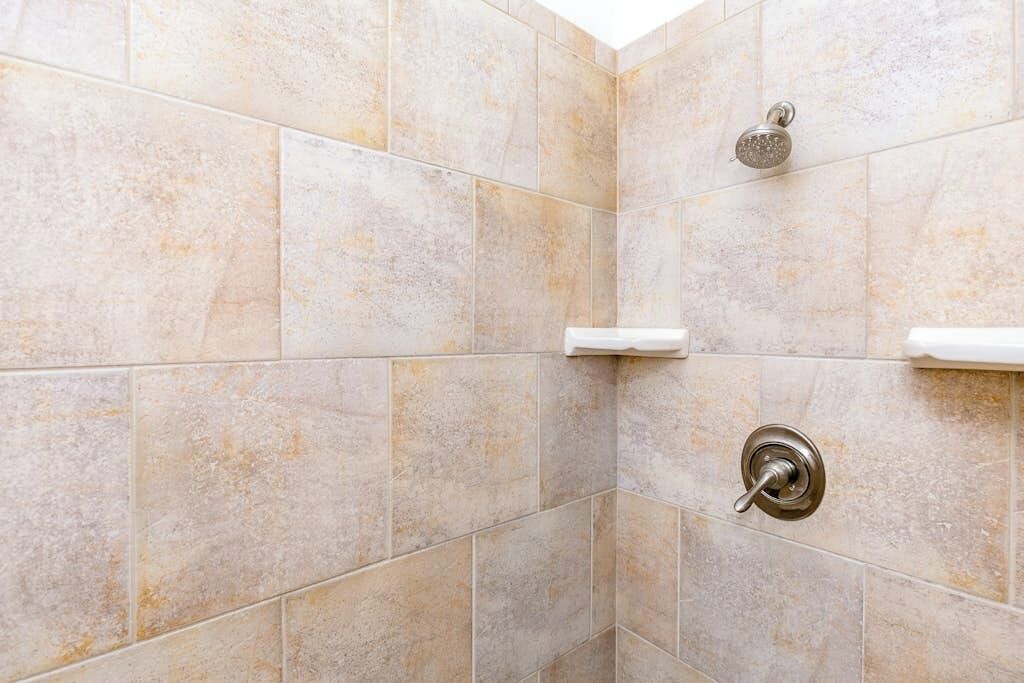 A shower area with beige tiles and a handheld showerhead.