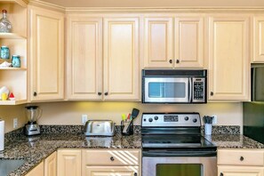 A kitchen with light wooden cabinets, a granite countertop, a toaster, a blender, and a stove. - Royal Sands Beauty - Walk to Beach, Pool Access (Port Aransas)