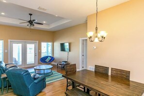 A spacious living area with a dining table, blue sofa, and a ceiling fan. - Royal Sands Beauty - Walk to Beach, Pool Access (Port Aransas)