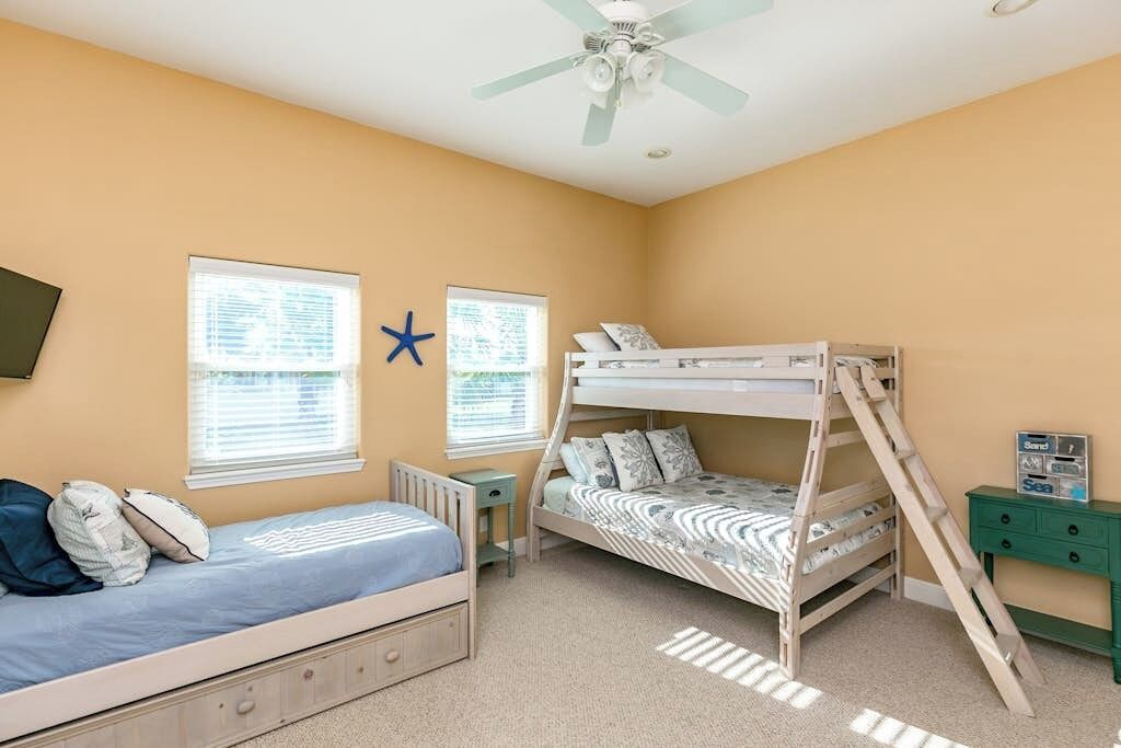 A child's bedroom with bunk beds, a desk, and a ceiling fan.