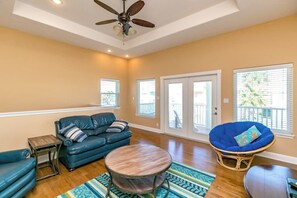A spacious living room with a ceiling fan, a blue sofa, a round coffee table, and a rattan chair. - Royal Sands Beauty - Walk to Beach, Pool Access (Port Aransas)