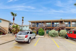 Ein mehrstöckiges Hotel mit Parkplatz, Treppe und einem roten Fahrzeug, das rechts geparkt ist.