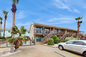 A multi-story building with balconies, a car parked in front, and palm trees. - Pirate's Crossing #B6 (Corpus Christi)