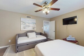 Ein Schlafzimmer mit Bett, Deckenventilator, Gemälde, Fernseher und einer Tür.