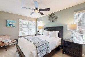 Ein Schlafzimmer mit Bett, Deckenventilator, Nachttisch, Lampe, Sessel und Wanddeko.