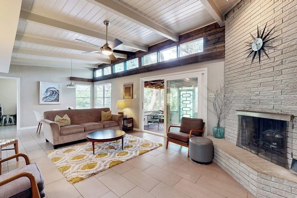 A spacious living room with a fireplace, a ceiling fan, and a large window.