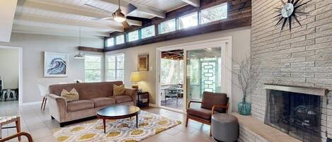 A spacious living room with a fireplace, a ceiling fan, and a large window.